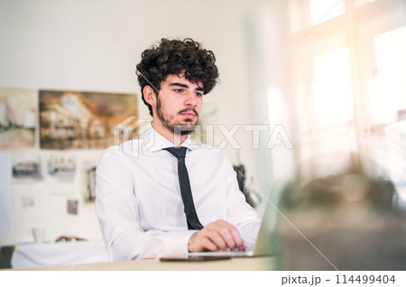 Young businessman working on new project in a startup company office. Working in co-working space. Young businessman working on new project in a startup company office. Working in co-working space. 114499404