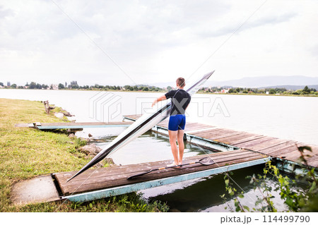 Young canoeist carry canoe and paddle, going into water, walking on wooden dock. Concept of canoeing as dynamic and adventurous sport Young canoeist carry canoe and paddle, going into water, walking on wooden dock. Concept of canoeing as dynamic and adventurous sport 114499790