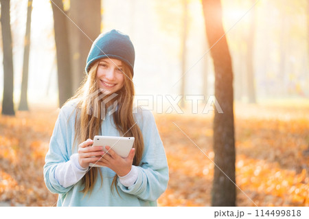 Nice girl holding tablet on autumnal background Nice girl holding tablet on autumnal background 114499818