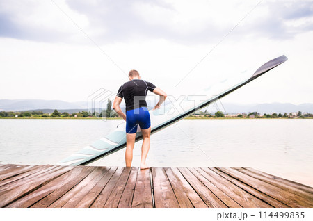 Young canoeist putting canoe into water, standing on wooden dock. Concept of canoeing as dynamic and adventurous sport 114499835