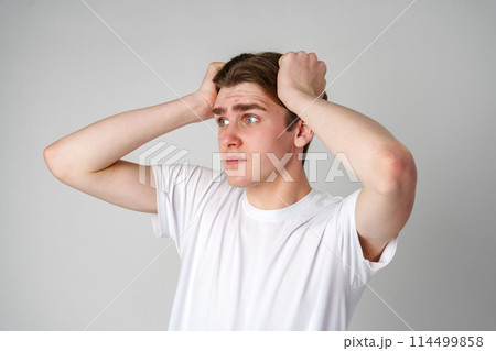 Young Man In White T-Shirt Looking Worried With Hands On Head Against Plain Background Young Man In White T-Shirt Looking Worried With Hands On Head Against Plain Background 114499858