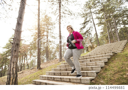 Overweight woman running in city park, down the stairs. Exercising outdoors for people with obesity. 114499881