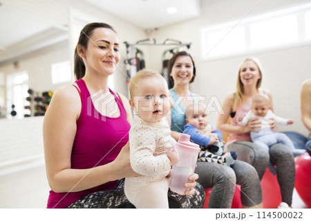 Baby movement class. Parents helping babies to improve motor skills, proper movement on fitball. Pediatric physical therapist leading class. Mothers exercising with babies. 114500022