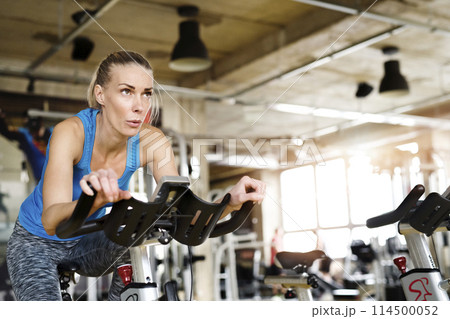 Beautiful sport woman cycling on stationary bike in gym. Routine workout for woman's physical and mental health. Beautiful sport woman cycling on stationary bike in gym. Routine workout for woman's physical and mental health. 114500052