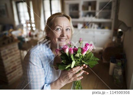 Beautiful mature woman arranging bouquet of roses in a vase, a hobby and relaxation. Older woman living alone, enjoying peaceful weekend day 114500308