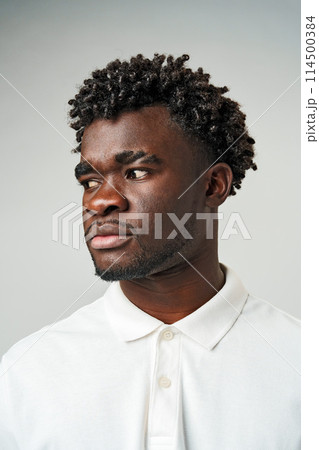 A young man with short curly hair looks thoughtfully off to the side. 114500384