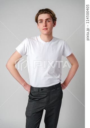 Young Man in White T-Shirt and Grey Trousers Posing Against a Plain Background Young Man in White T-Shirt and Grey Trousers Posing Against a Plain Background 114500405