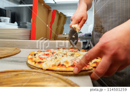 Chef Cutting Freshly Baked Pizza in a Commercial Kitchen Setting 114501259