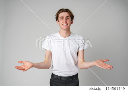 Young Man in White T-Shirt Gesturing With Open Arms Against a Plain Background Young Man in White T-Shirt Gesturing With Open Arms Against a Plain Background 114501349