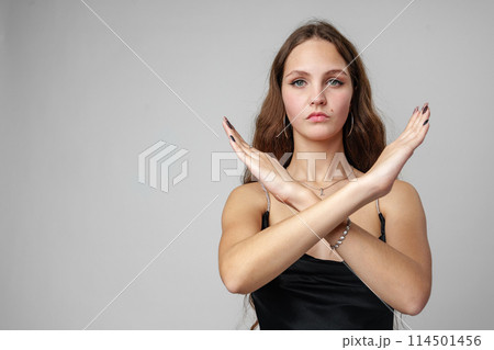 Young Woman in Elegant Black Dress Making an X Sign With Her Arms Against a Grey Background Young Woman in Elegant Black Dress Making an X Sign With Her Arms Against a Grey Background 114501456