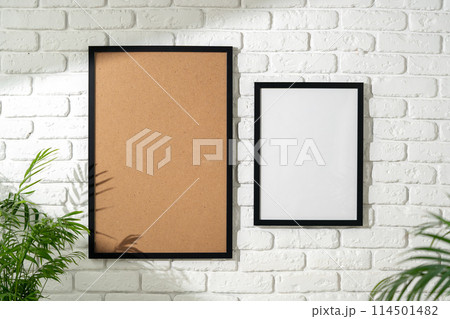 Two Empty Picture Frames Hanging on a White Brick Wall With a Plant in the Foreground Two Empty Picture Frames Hanging on a White Brick Wall With a Plant in the Foreground 114501482