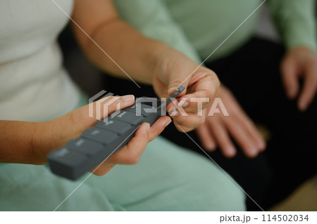 Closeup mature woman taking medicine from pill organizer box. Health care, medicine and treatment concept Closeup mature woman taking medicine from pill organizer box. Health care, medicine and treatment concept 114502034