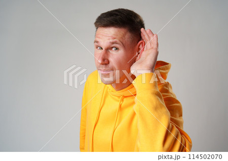 Portrait of young casual man with hand on ear who overhears on gray background Portrait of young casual man with hand on ear who overhears on gray background 114502070