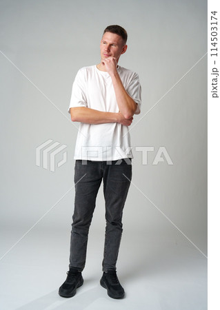 Thoughtful caucasian young male touching chin with hand thinking on gray background Thoughtful caucasian young male touching chin with hand thinking on gray background 114503174