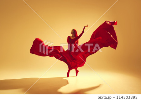 Artistic and deep performance Woman, female dancer in flowing red dress dancing against golden color background Artistic and deep performance Woman, female dancer in flowing red dress dancing against golden color background 114503895