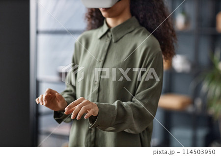 Selective focus shot of unrecognizable girl in VR headset standing indoors typing on virtual keyboard in air, copy space Selective focus shot of unrecognizable girl in VR headset standing indoors typing on virtual keyboard in air, copy space 114503950
