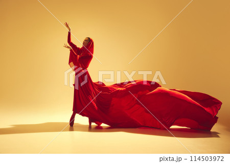 Passion in motion. Beautiful woman, dancer in flowing elegant red dress making powerful performance against sand color background Passion in motion. Beautiful woman, dancer in flowing elegant red dress making powerful performance against sand color background 114503972