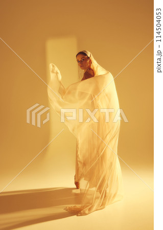 Ethereal beauty. Mystical scene of female ballet dancer with golden flowing fabric performing, symbolizing purity and elegance of ballet 114504053