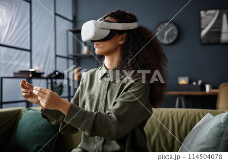 Young biracial woman with curly hair wearing VR headset working or playing video game in living room at home Young biracial woman with curly hair wearing VR headset working or playing video game in living room at home 114504078