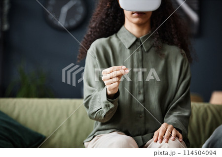 Medium crop shot of unrecognizable woman sitting on sofa in living room using VR headset, copy space Medium crop shot of unrecognizable woman sitting on sofa in living room using VR headset, copy space 114504094