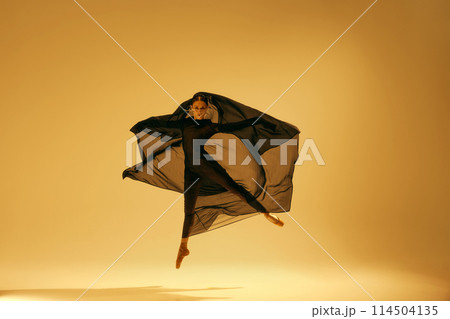 Artistic dance expression. Beautiful ballerina with golden accessories, in black costume dancing against yellow studio background 114504135