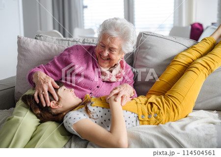 Cute girl lying head on gradmother knees. Portrait of an elderly woman spending time with granddaughter. Cute girl lying head on gradmother knees. Portrait of an elderly woman spending time with granddaughter. 114504561