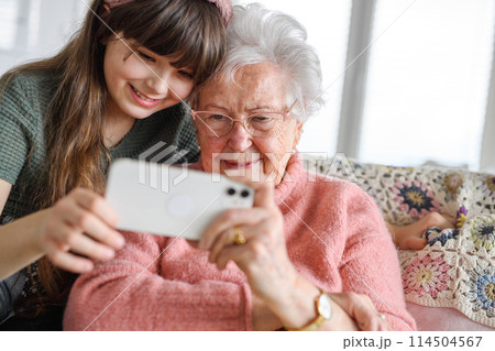 Grandmother with cute girl taking selfie with smartphone. Portrait of an elderly woman spending time with granddaughter. Grandmother with cute girl taking selfie with smartphone. Portrait of an elderly woman spending time with granddaughter. 114504567
