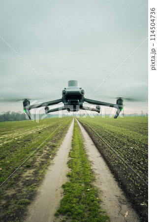 Aerial view of a drone moderning over farm fields, monitoring, analyzing crop health. Agricultural drone in modern farming. 114504736