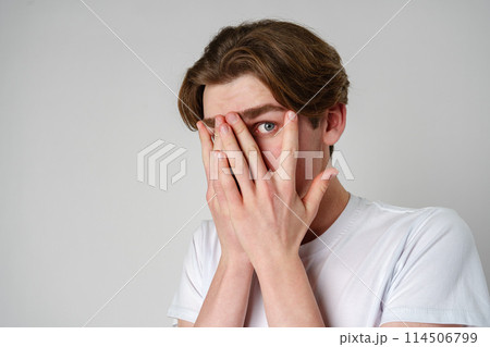 Young Man Covering His Face With His Hands Against a Neutral Background 114506799