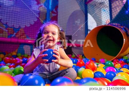 Joyful Young Girl Playing in a Colorful Ball Pit at an Indoor Playground 114506996