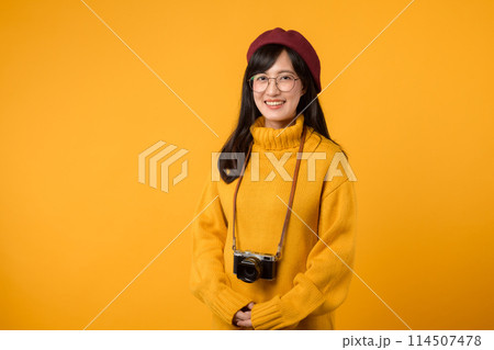 With her camera, a young Asian woman, donned in a yellow sweater and red beret, takes a portrait, showcasing her artistic pursuit. 114507478