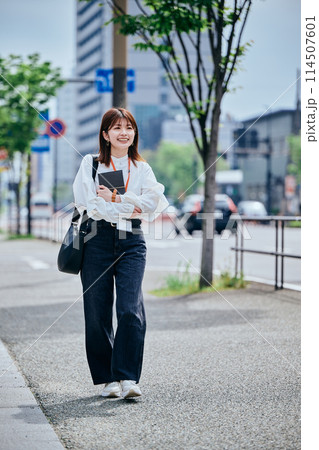 手帳を胸に抱えて歩く若い女性 手帳を胸に抱えて歩く若い女性 114507601