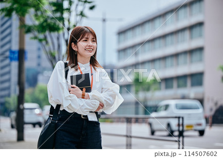手帳を胸に抱えて歩く若い女性 手帳を胸に抱えて歩く若い女性 114507602