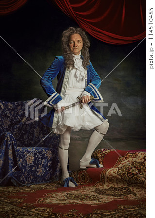 Medieval person, senior man posing wearing old-fashioned clothes posing with sword against vintage studio background. 114510485