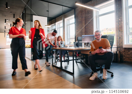 A diverse group of business professionals collaborates in a modern startup coworking center, utilizing a mix of paper-based and technological tools such as mobile phones and computers  114510692