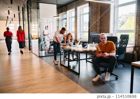 A diverse group of business professionals collaborates in a modern startup coworking center, utilizing a mix of paper-based and technological tools such as mobile phones and computers  114510698