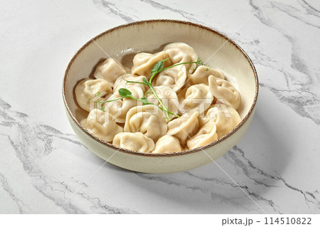 Bowl of freshly boiled dumplings with greens on marbled surface Bowl of freshly boiled dumplings with greens on marbled surface 114510822