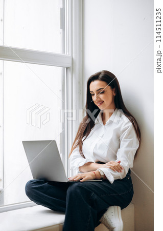 Business lady sitting on windowsill and using laptop. Finance manager working in office.  Business lady sitting on windowsill and using laptop. Finance manager working in office.  114511235