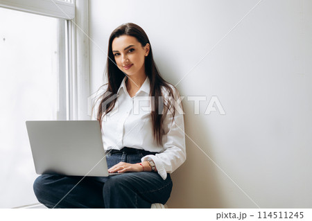 Business lady sitting on windowsill and using laptop. Finance manager working in office. Place for text  114511245
