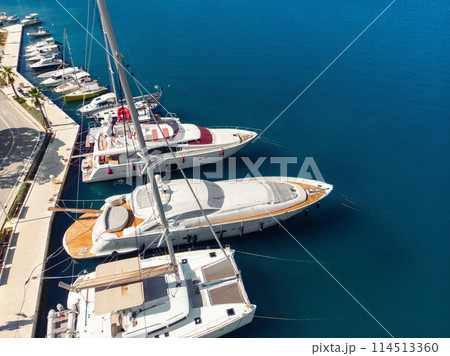 Scenic aerial view many yachts boats moored at Croatian bay harbor shore blue turquoise clear water at bright summer sunny day. Top above Mediterranean sea marina. Boat vessel charter service Scenic aerial view many yachts boats moored at Croatian bay harbor shore blue turquoise clear water at bright summer sunny day. Top above Mediterranean sea marina. Boat vessel charter service 114513360