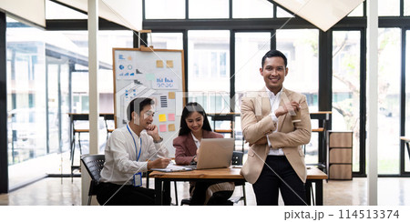 Smiling confident businessman looking at camera and standing in an office at team meeting. Portrait of confident businessman with colleagues in boardroom 114513374