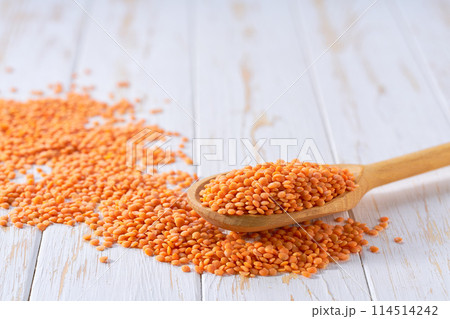 Raw red lentils crumble from in a wooden spoon on a white wooden table. 114514242