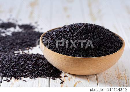 raw black rice are scattered out of the wooden bowl on a light table, selective focus. raw black rice are scattered out of the wooden bowl on a light table, selective focus. 114514249