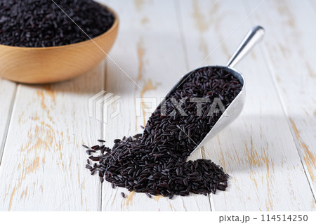 Organic raw black rice in a metal scoop on a white wooden table. Organic raw black rice in a metal scoop on a white wooden table. 114514250