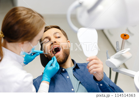 A handsome man is sitting in a chair at a woman's appointment at the dentist's office A handsome man is sitting in a chair at a woman's appointment at the dentist's office 114514363