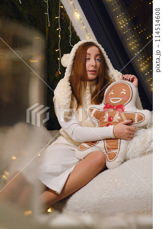 Merry young fun woman wearing white warm sweater hat posing hold ginger cookie man pillow studio portrait. Happy New Year celebration holiday concept Merry young fun woman wearing white warm sweater hat posing hold ginger cookie man pillow studio portrait. Happy New Year celebration holiday concept 114514608