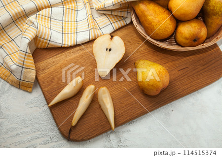 Cutting board with whole and slices pears, wicker basket and yellow kitchen towel on white wooden background.. Cutting board with whole and slices pears, wicker basket and yellow kitchen towel on white wooden background.. 114515374