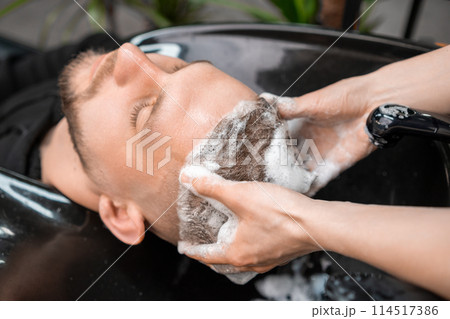 Hairstylist gives relaxing head massage to client washing hair in barbershop. Professional care of customer hairstyle. Spa procedure Hairstylist gives relaxing head massage to client washing hair in barbershop. Professional care of customer hairstyle. Spa procedure 114517386