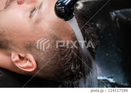 Hairdresser washes man hair from shampoo with warm water in barbershop closeup. Barber takes care of male client hair in professional salon Hairdresser washes man hair from shampoo with warm water in barbershop closeup. Barber takes care of male client hair in professional salon 114517399