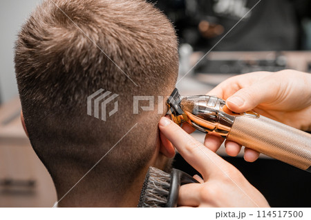 Barber shaves male client hair with trimmer in barbershop. Hairdresser shaving a mans temple 114517500